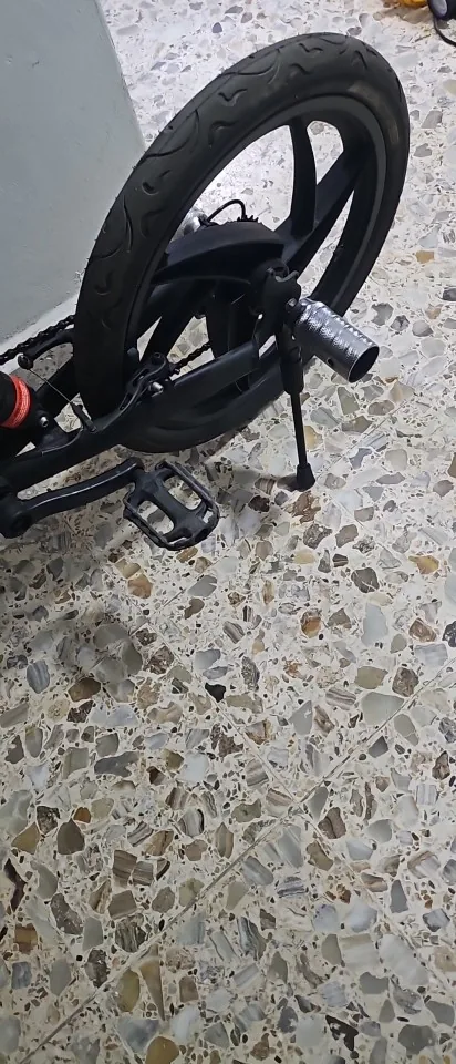 The kickstand deployed under the rear wheel of a black 20-inch bike, holding it upright on a terrazzo floor, photographed by a verified buyer
