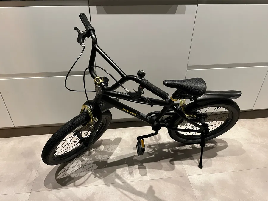 A black junior bike held upright by the kickstand on a tiled floor